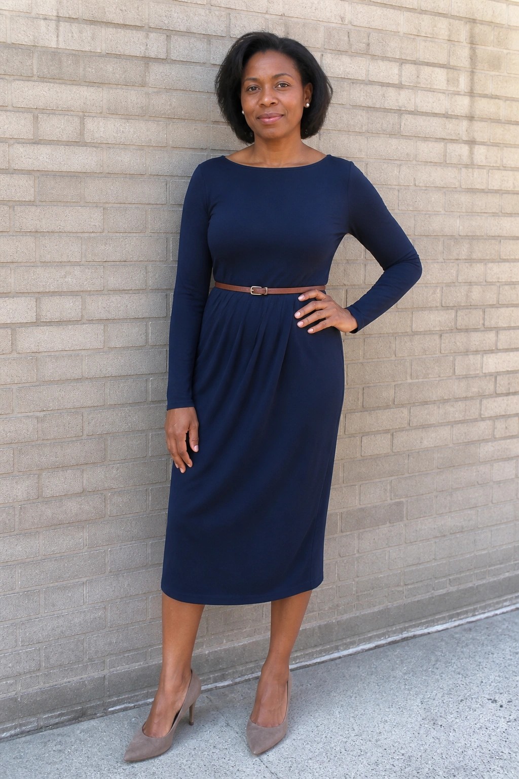 Woman in navy blue dress with brown belt posing by brick wall