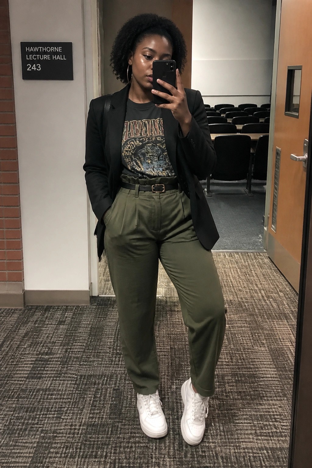Woman in black blazer and olive pants taking selfie in lecture hall doorway