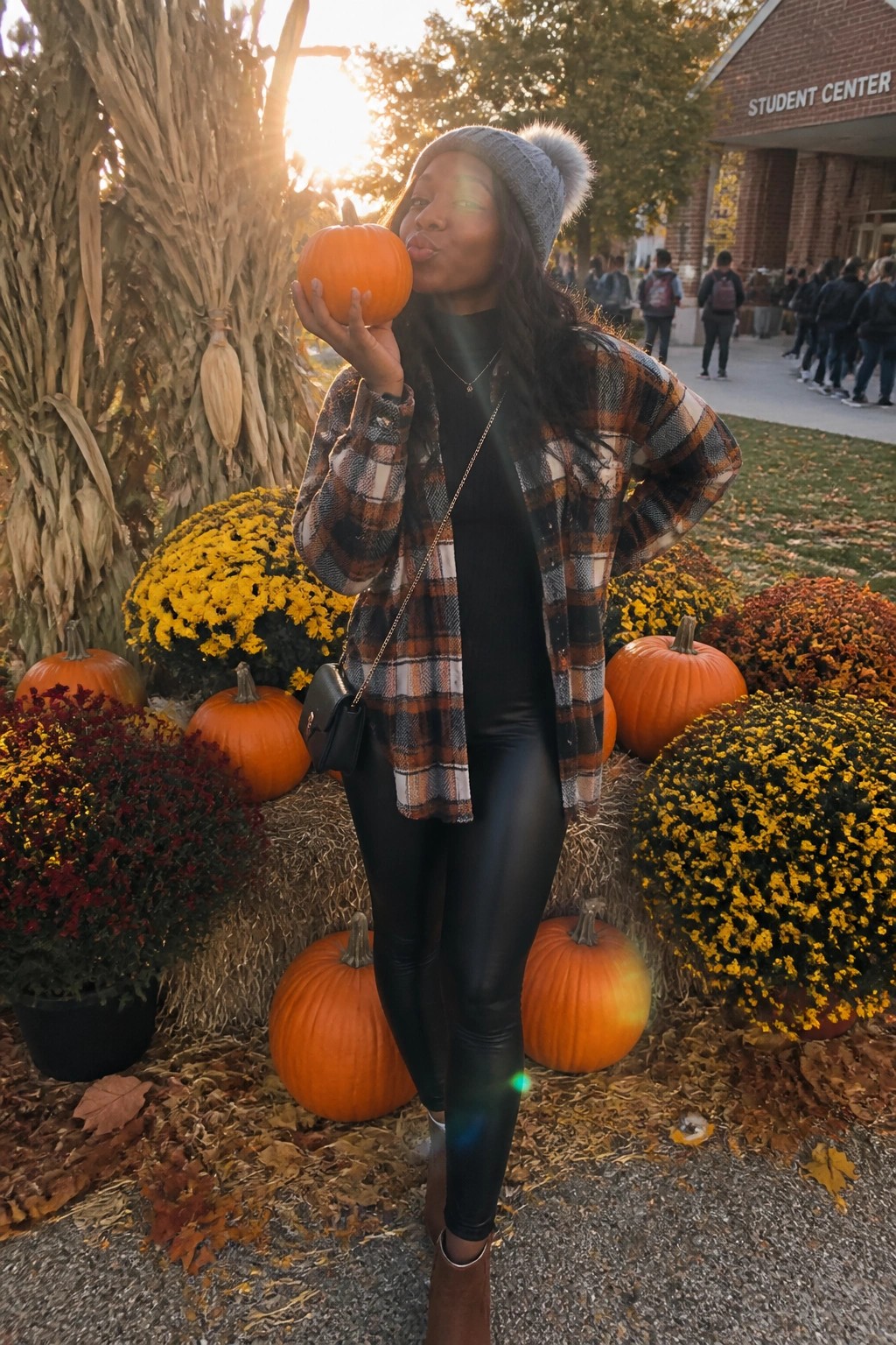 Woman in plaid flannel and beanie puckering lips with pumpkin amid autumn flowers