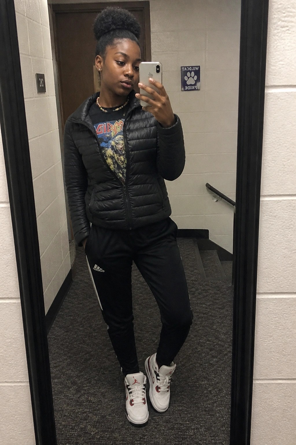 Woman in black puffer vest, graphic tee, Adidas pants, and Jordans takes mirror selfie