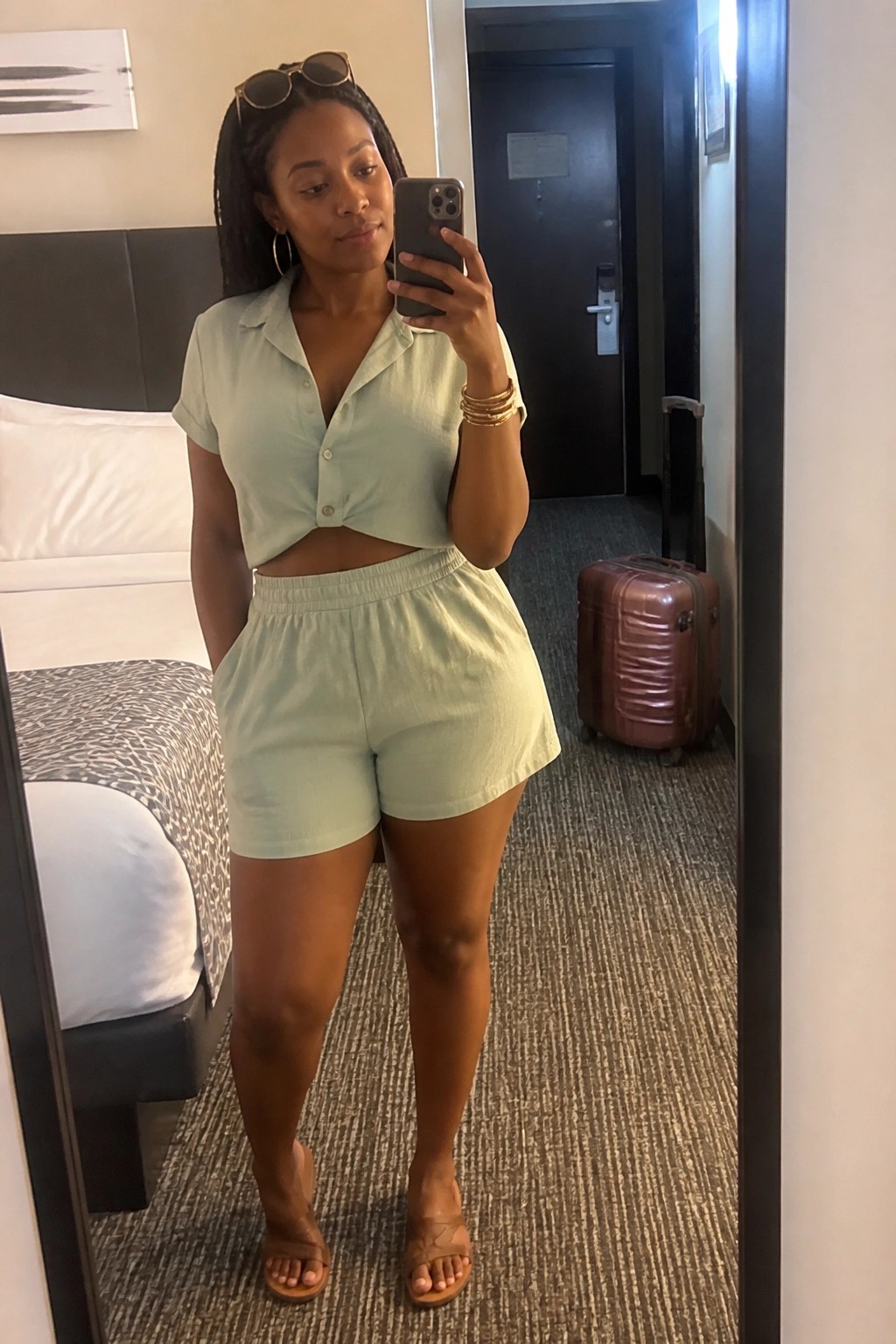 Woman in light green crop top and shorts taking mirror selfie in hotel room