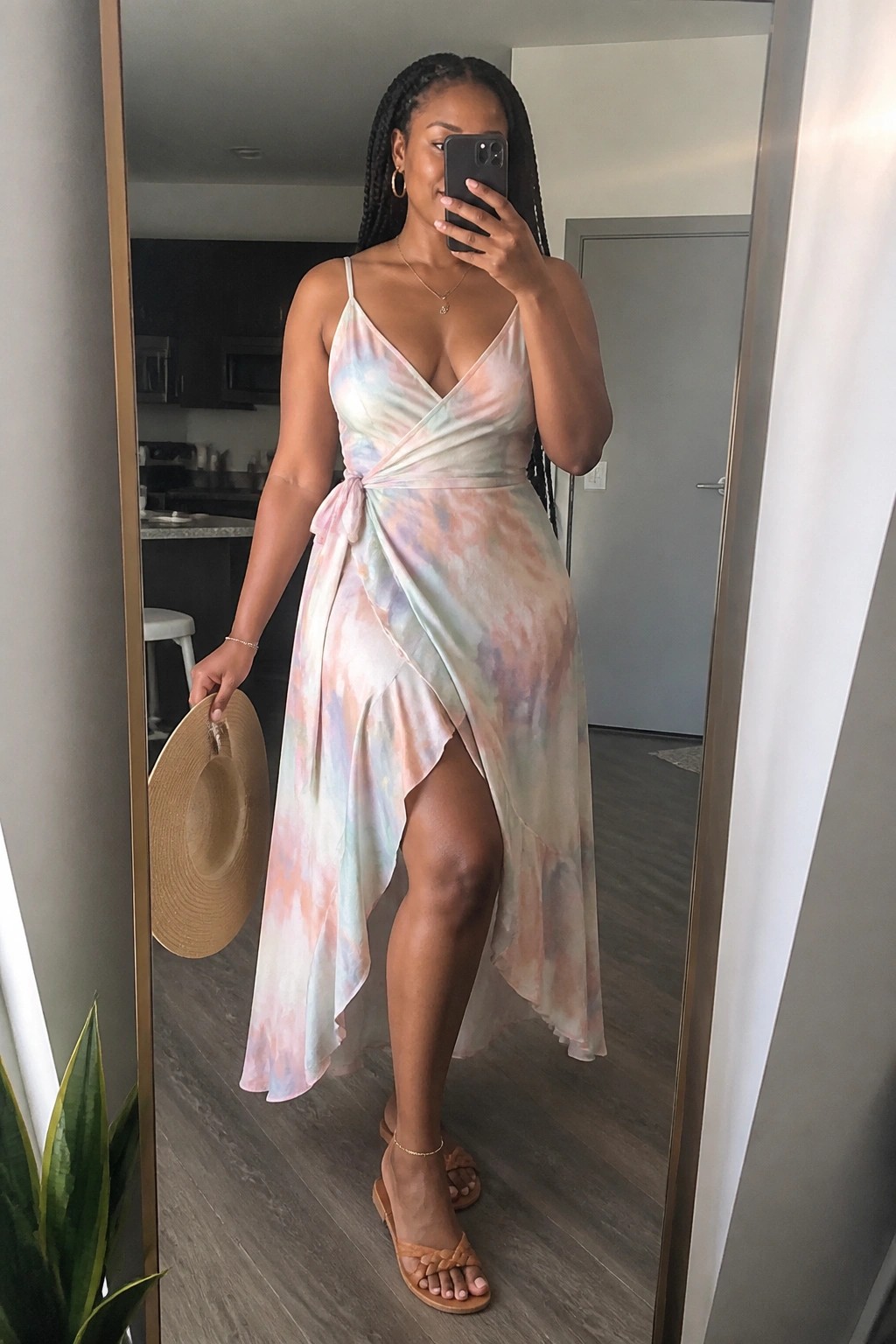 Woman in pastel tie-dye wrap dress holding phone and straw hat in mirror selfie