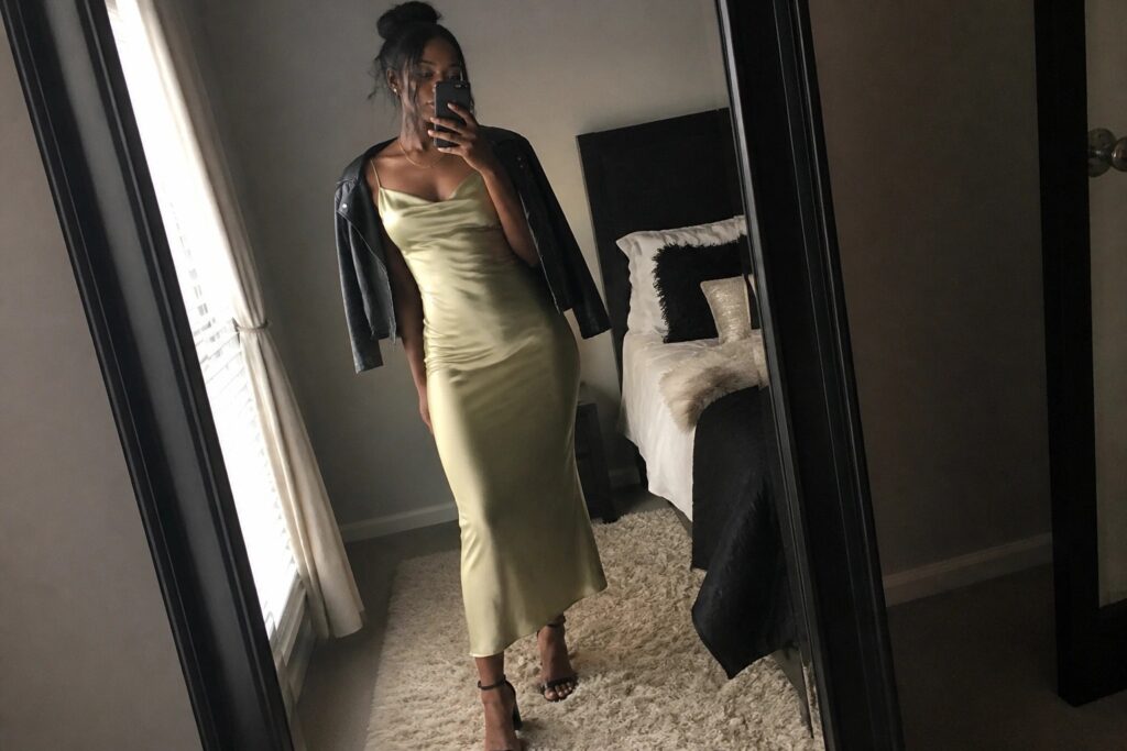 20 Night Out Outfits for Black Women Made for Dinner and Dancing Woman in long mauve satin dress and black leather jacket taking mirror selfie.