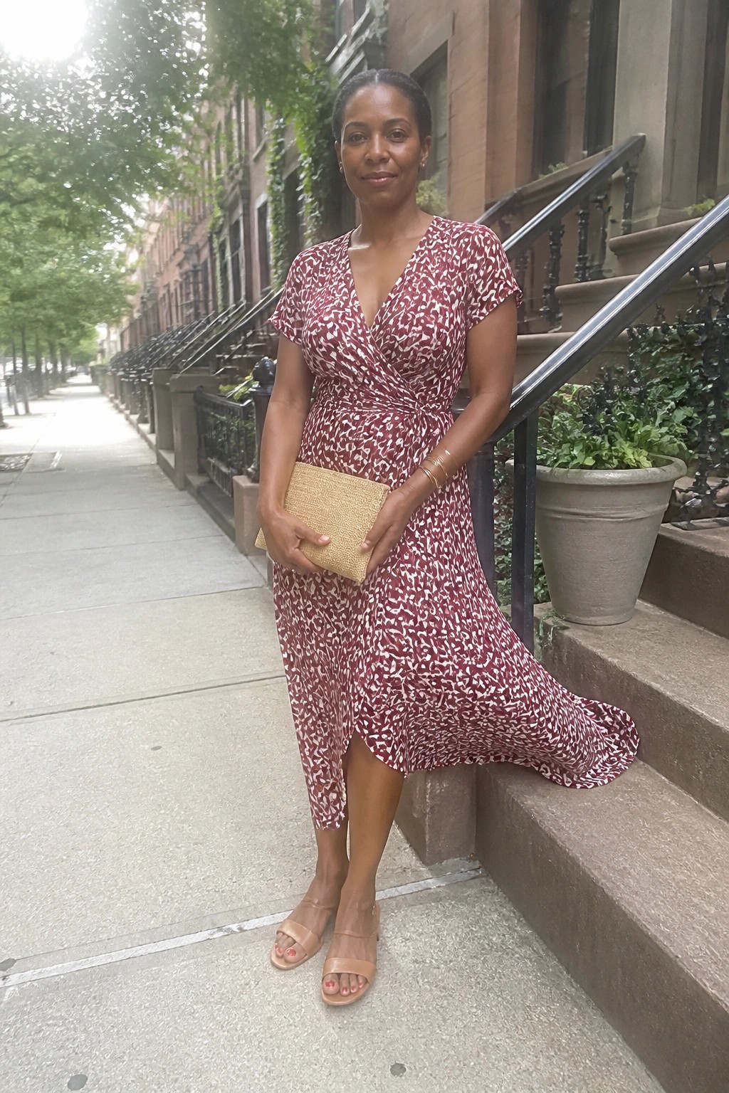 Woman in red floral wrap dress holding gold clutch on brownstone steps