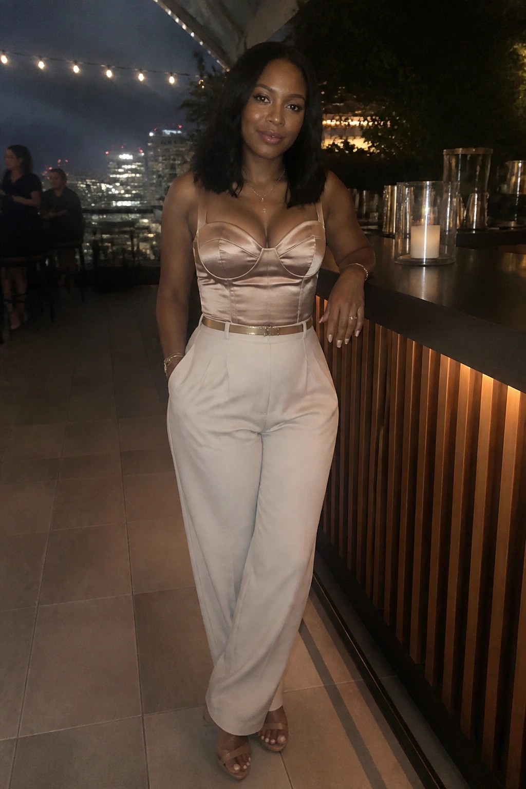 Woman in strapless satin top and wide-leg pants at nighttime rooftop bar