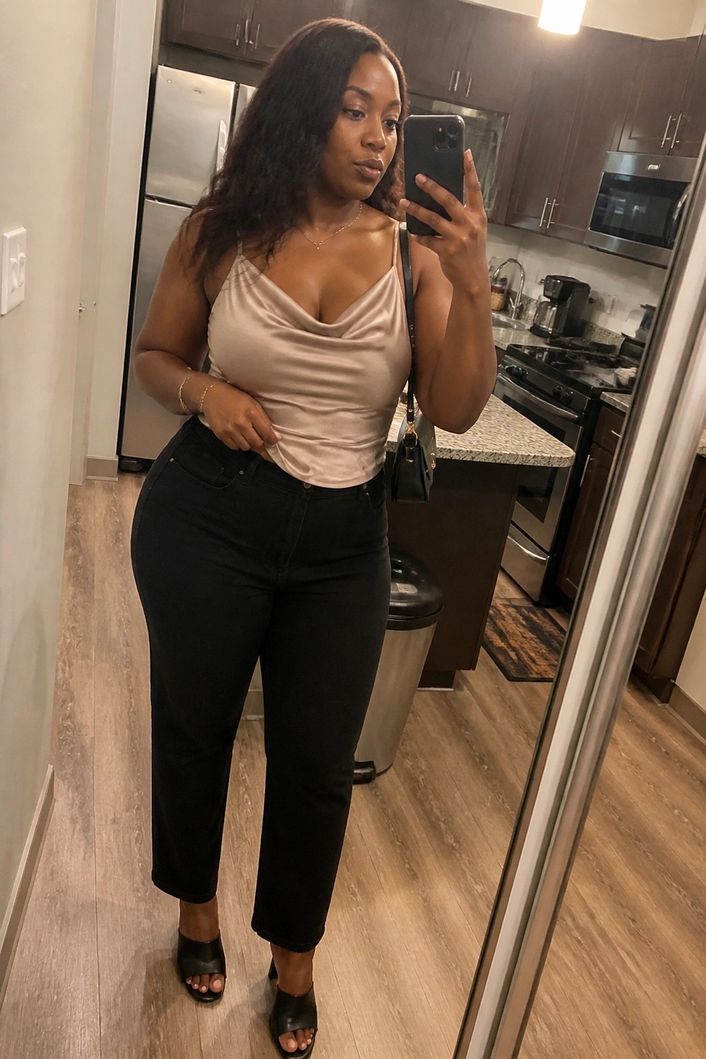 Woman in beige satin top and black jeans taking kitchen mirror selfie