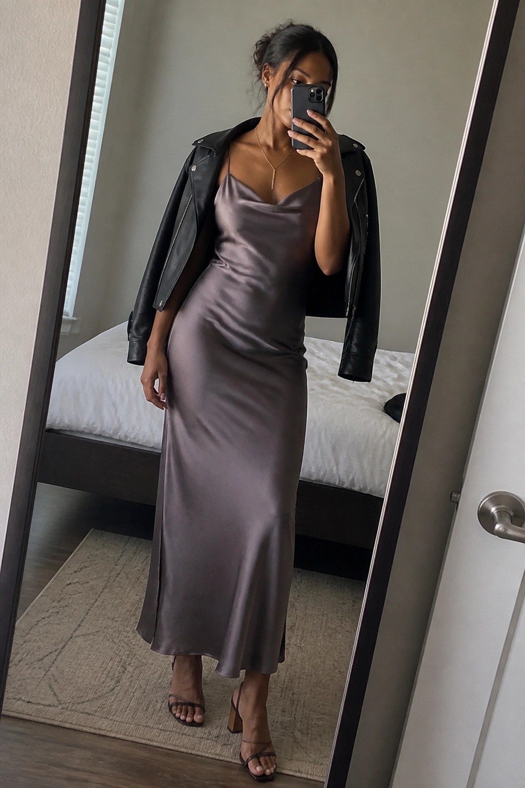Woman in long mauve satin dress and black leather jacket taking mirror selfie.