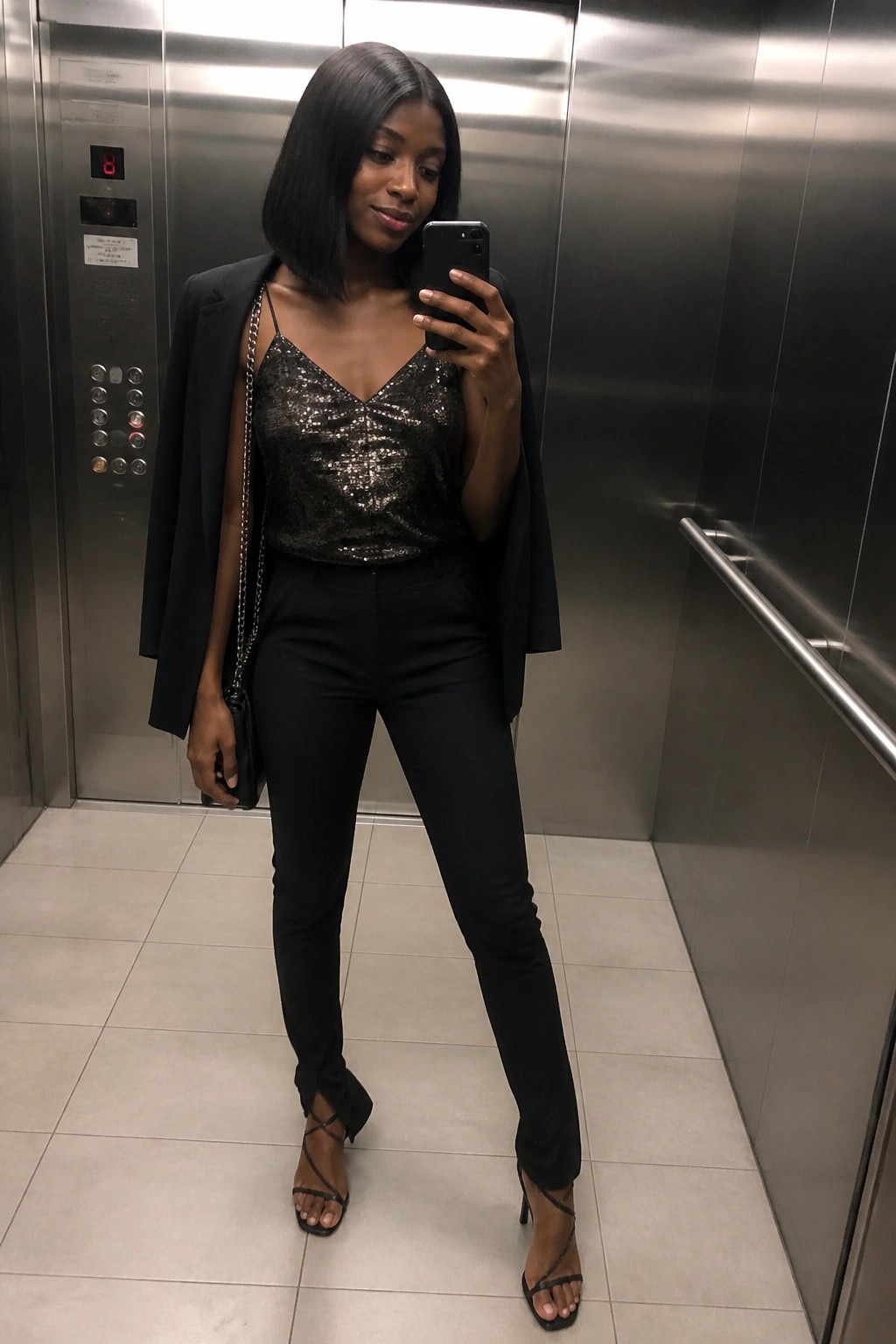 Woman in black sequined top and blazer taking selfie in elevator