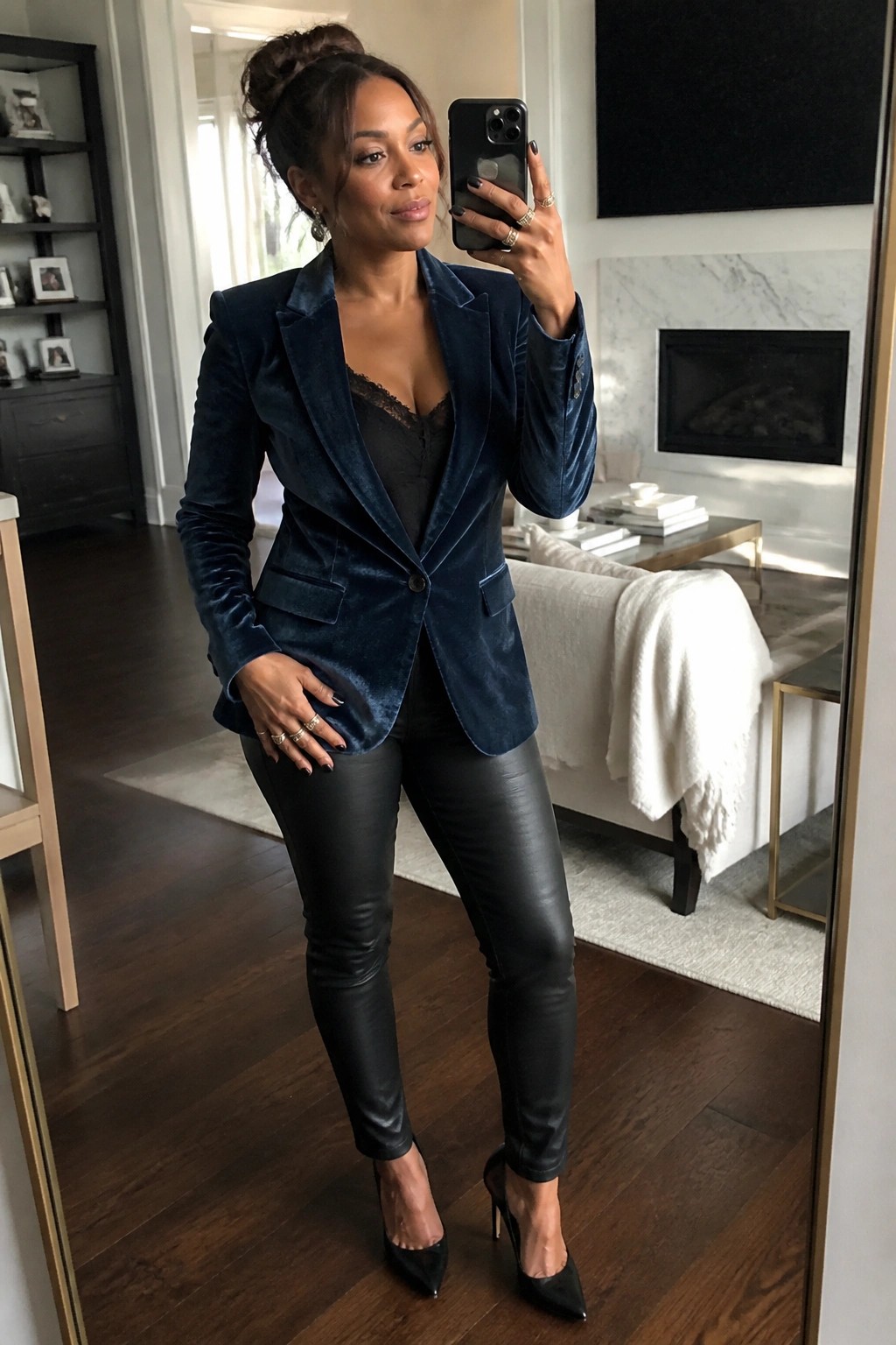 Woman in navy velvet blazer and black leather pants taking mirror selfie in living room