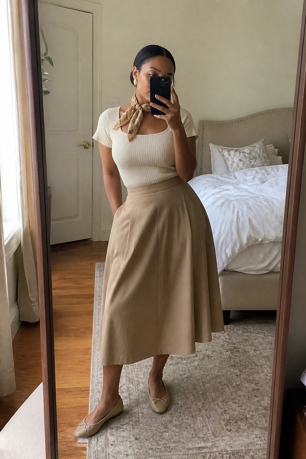 Woman taking a mirror selfie in a cream ribbed square neck short sleeve top with a beige patterned scarf tied at the neck, paired with a tan A line midi skirt and beige bow ballet flats.