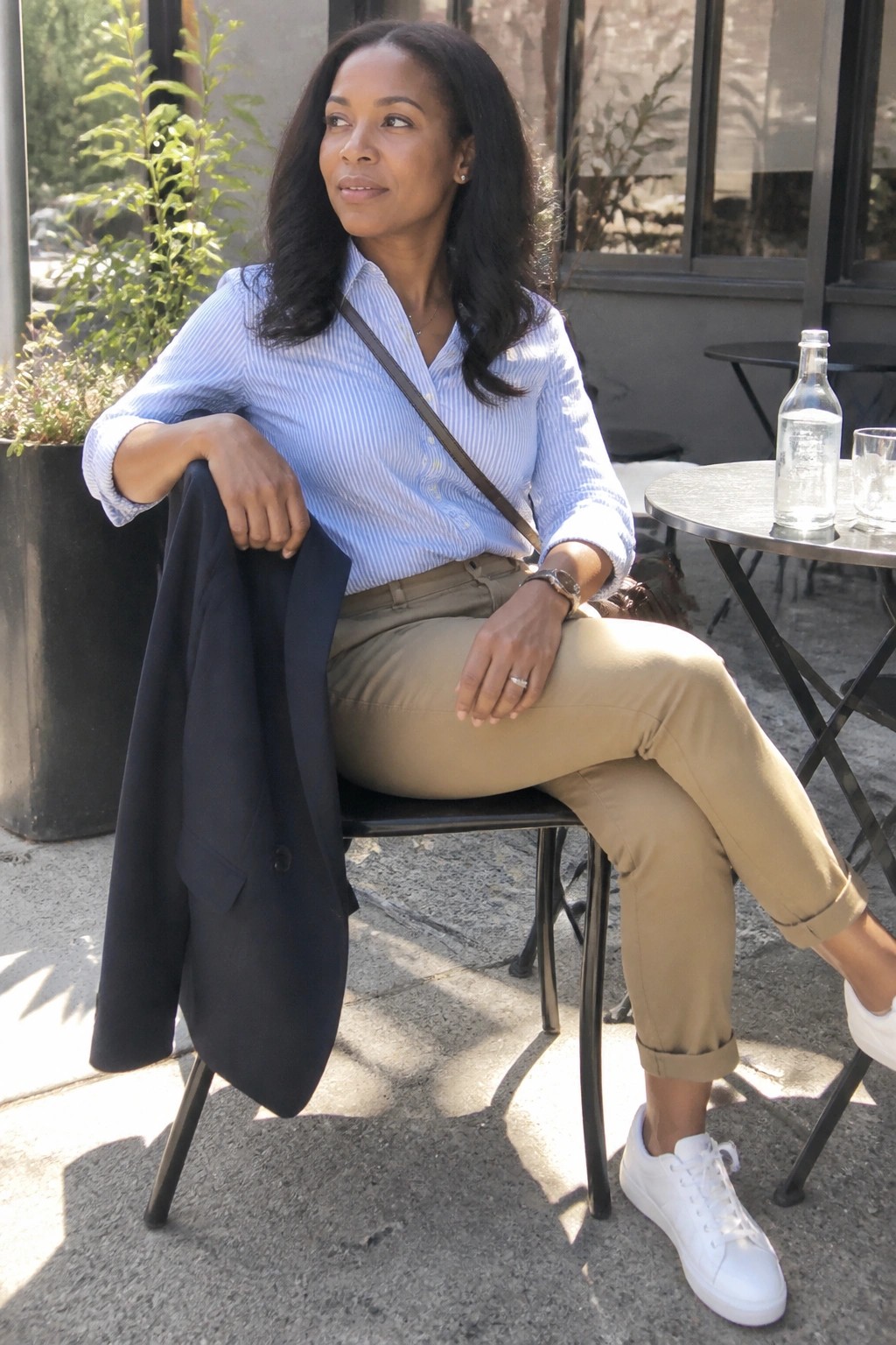 Woman in striped shirt and khaki pants holding navy blazer at outdoor table