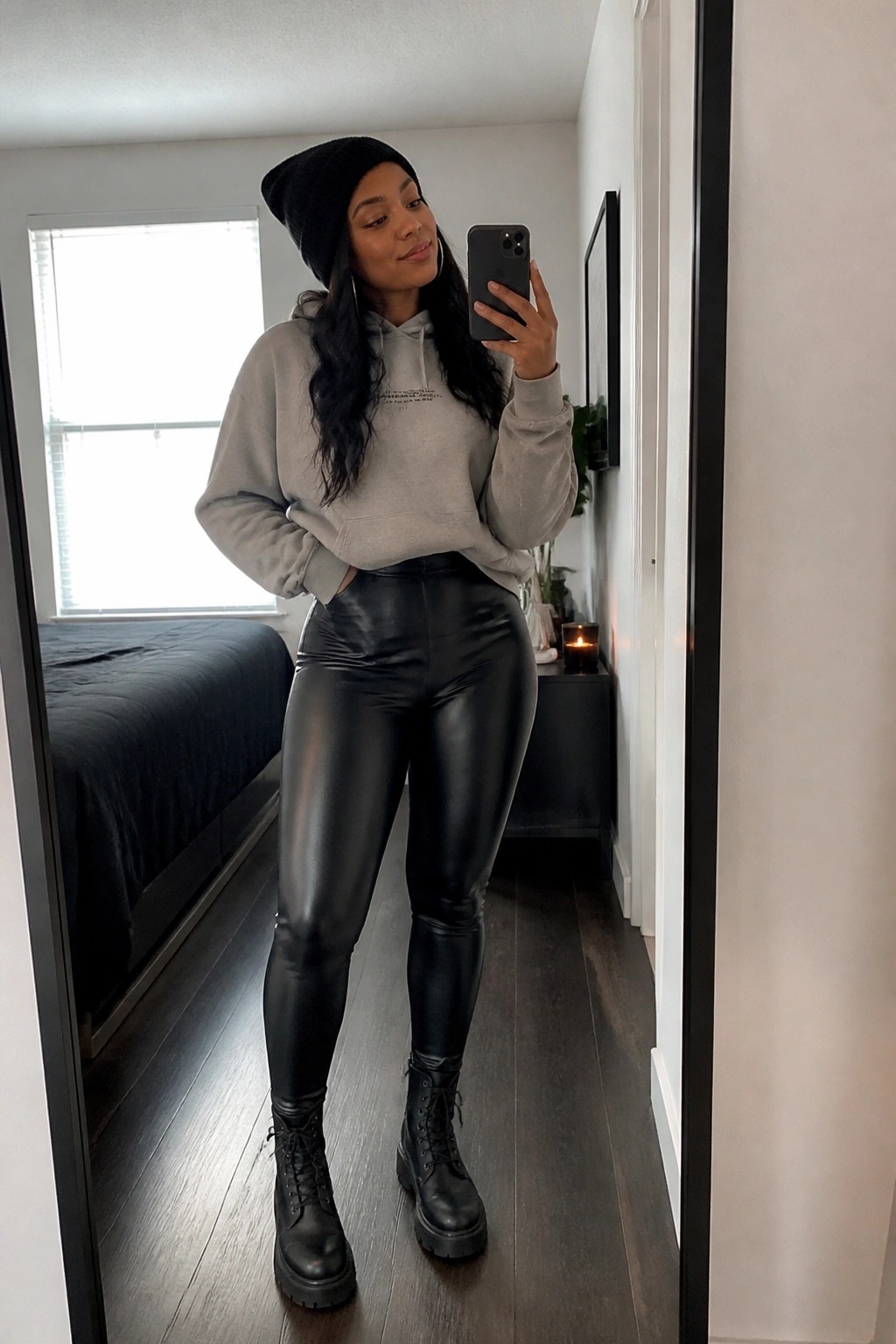 Woman in gray hoodie, black beanie, and shiny leggings taking mirror selfie.