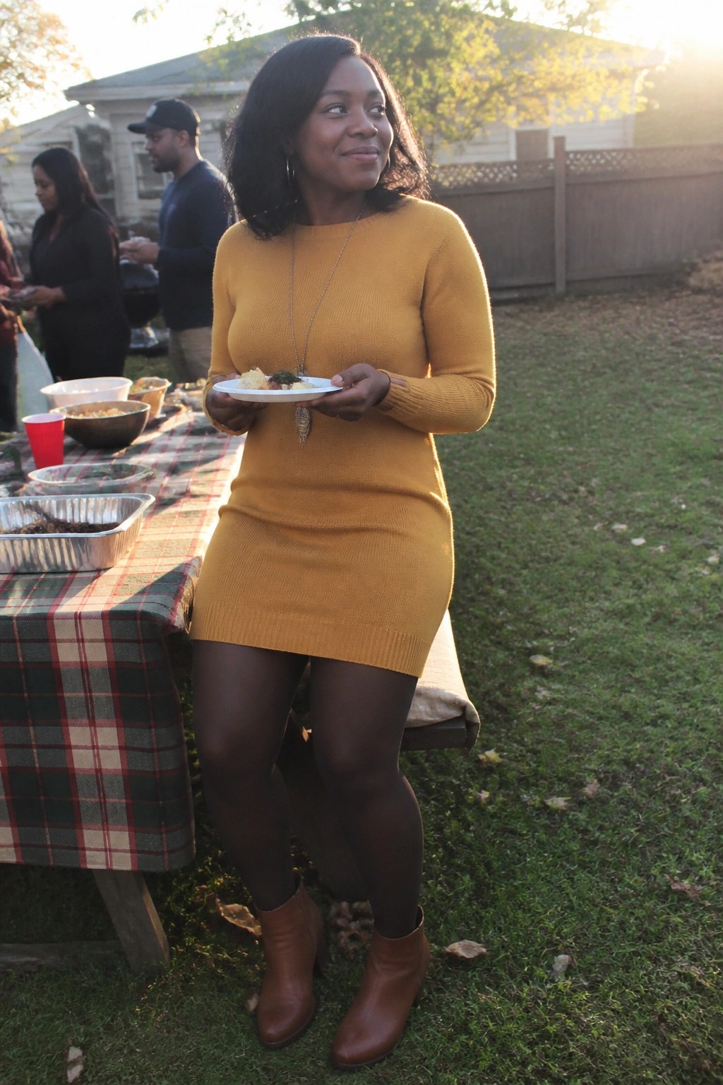 Woman in mustard-yellow knit dress holding food plate at backyard picnic