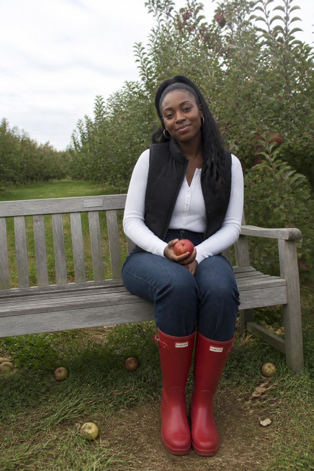 Woman in red boots holds apple on bench in apple orchard