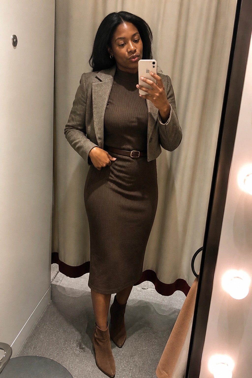 Woman in brown ribbed dress and gray blazer taking mirror selfie in fitting room