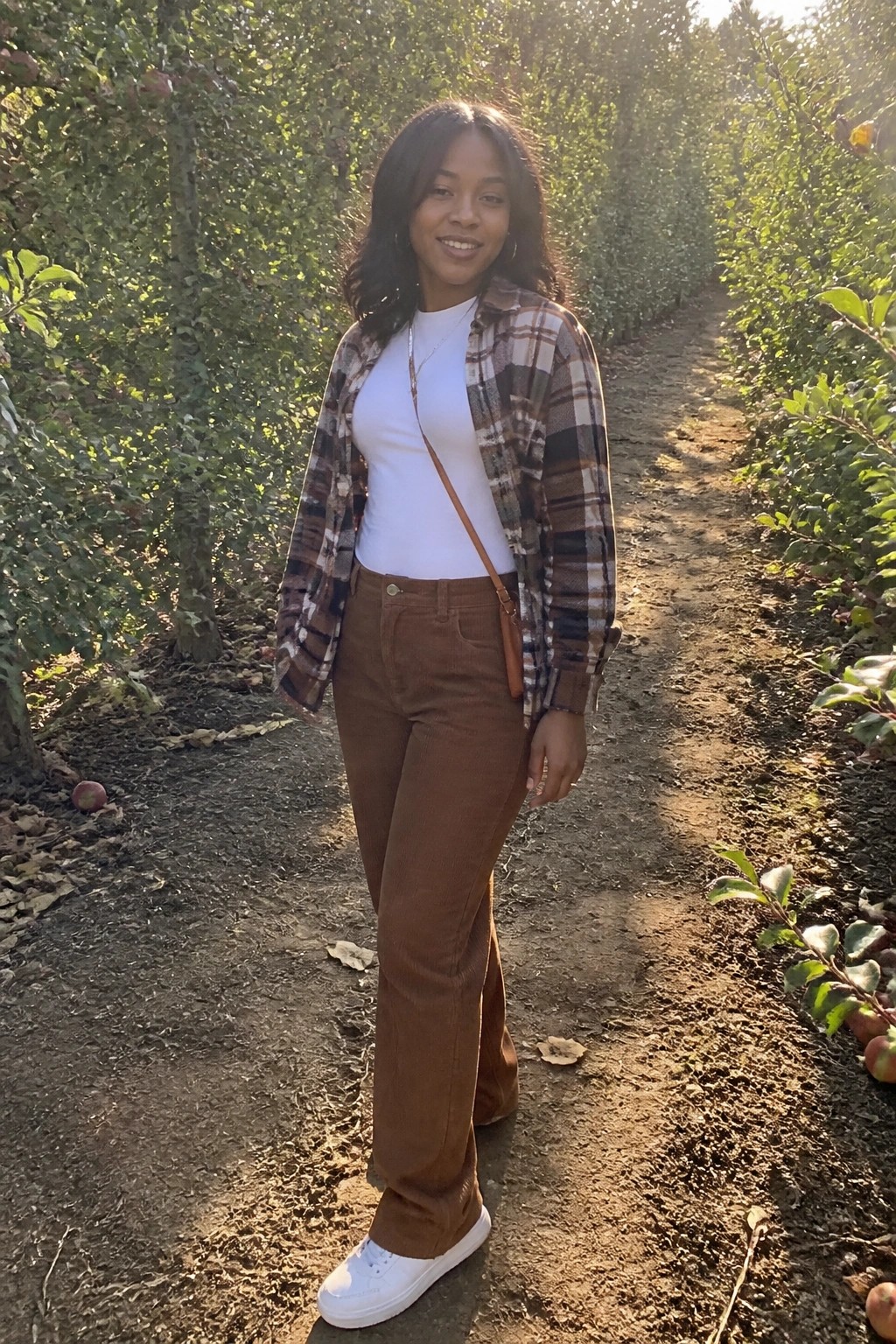 Woman in plaid shirt and brown pants on sunny orchard path