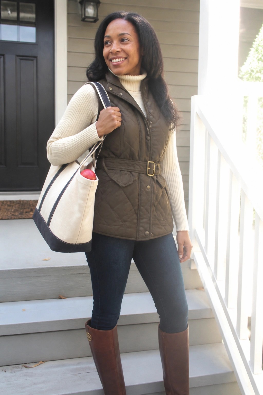 Smiling woman in brown quilted vest holding canvas tote bag on porch steps