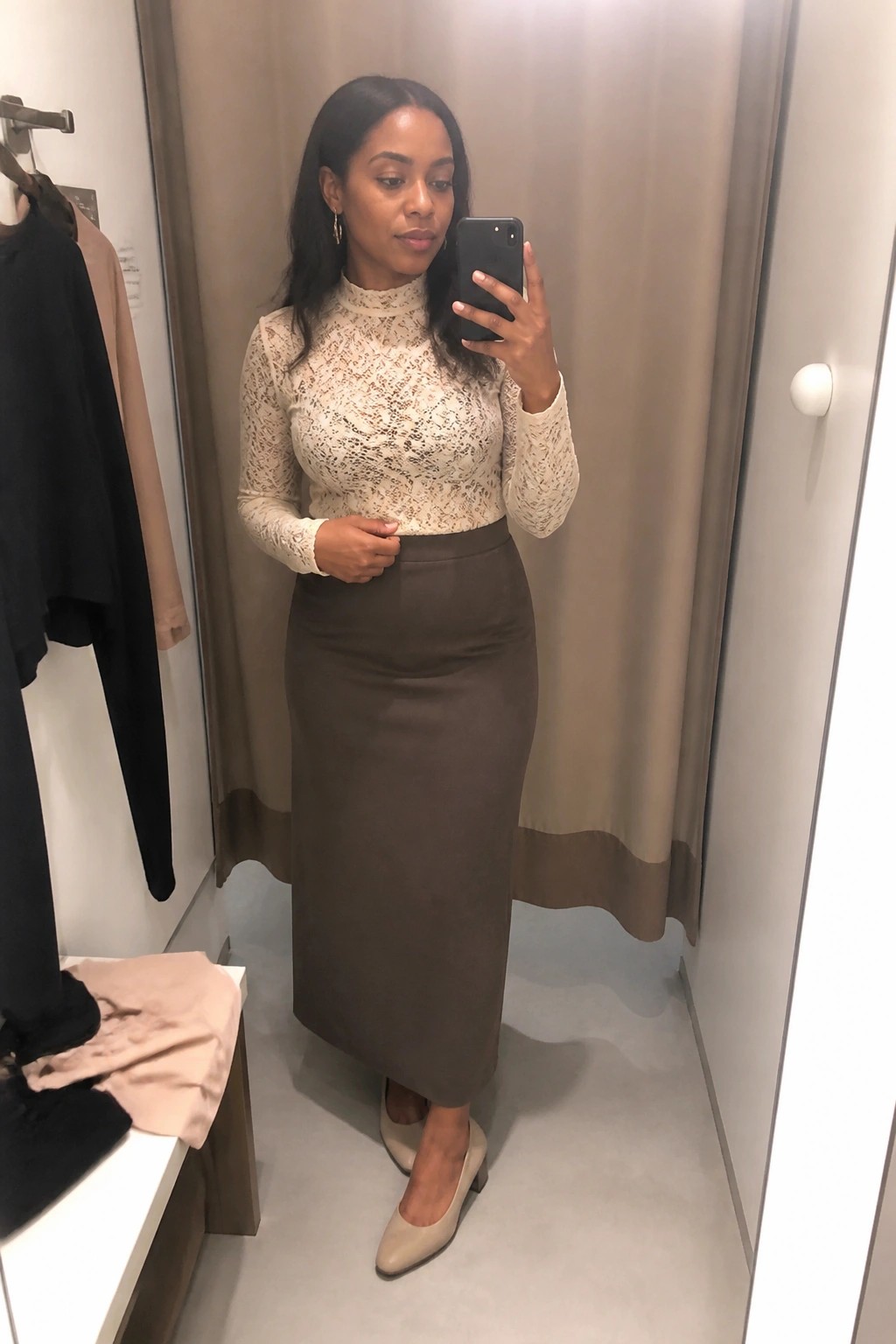 Woman in lace top and brown skirt taking mirror selfie in fitting room
