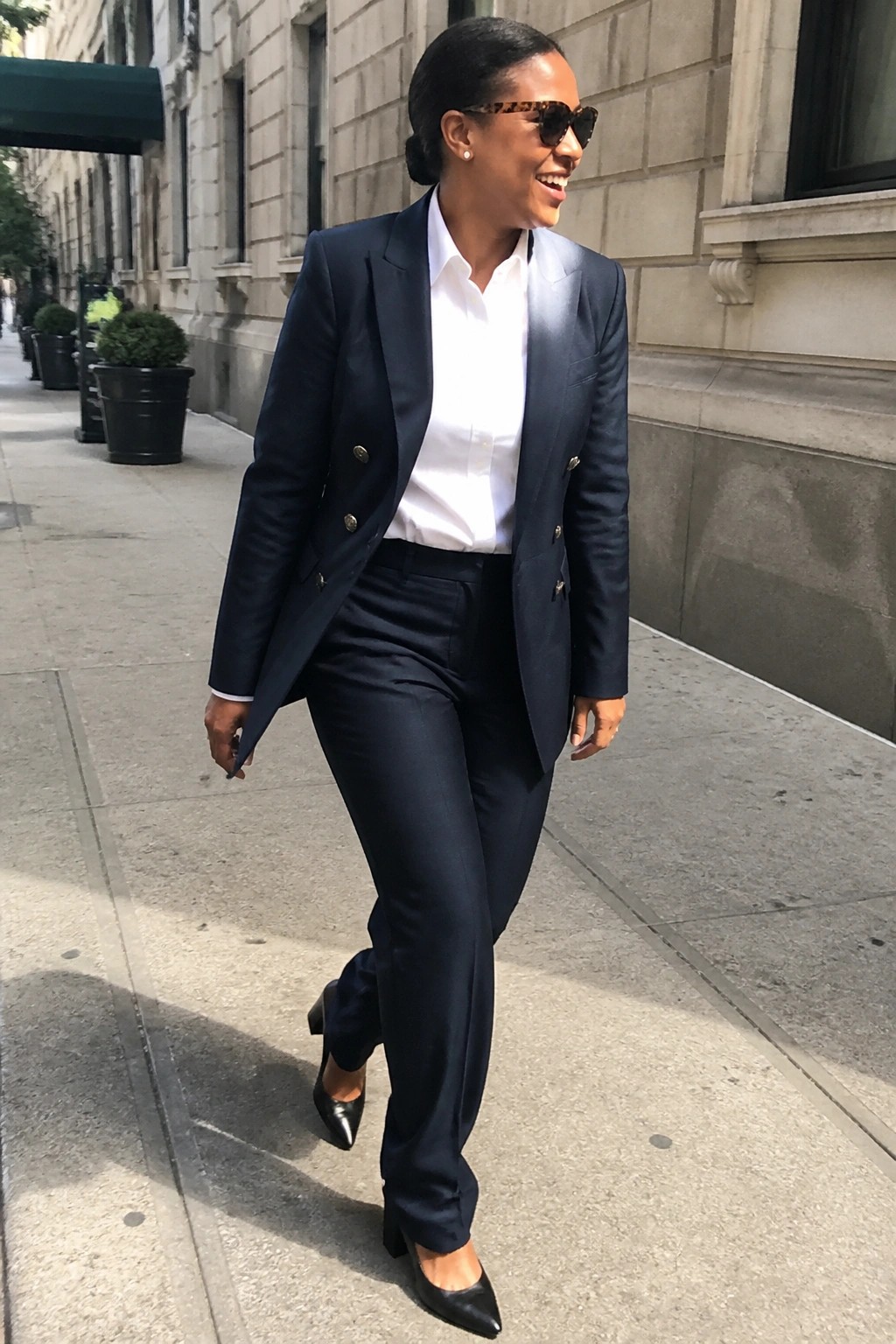 Woman in navy pantsuit and white shirt walking on sunny city sidewalk