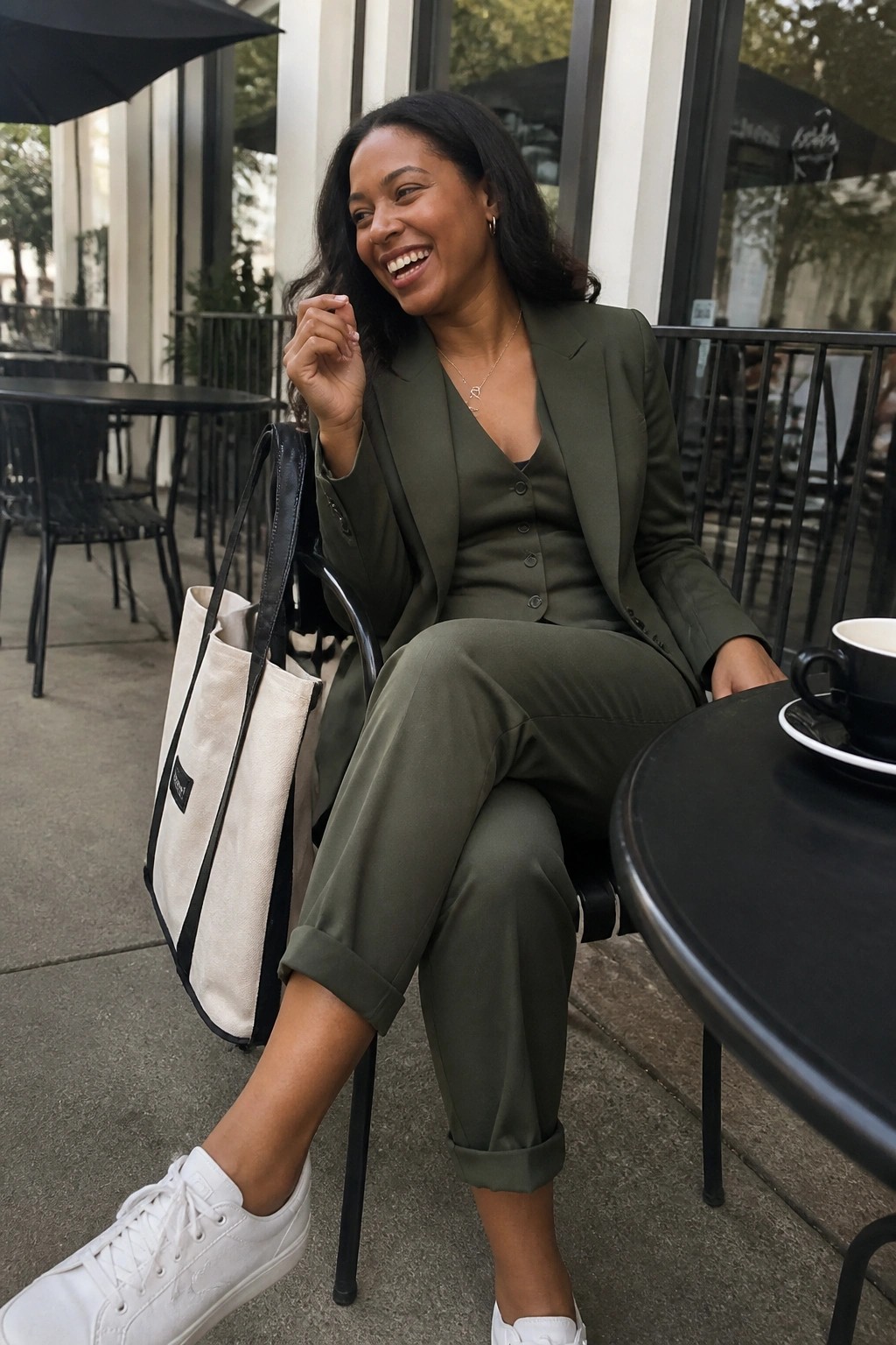 Smiling woman in olive green suit with tote bag and coffee at outdoor cafe