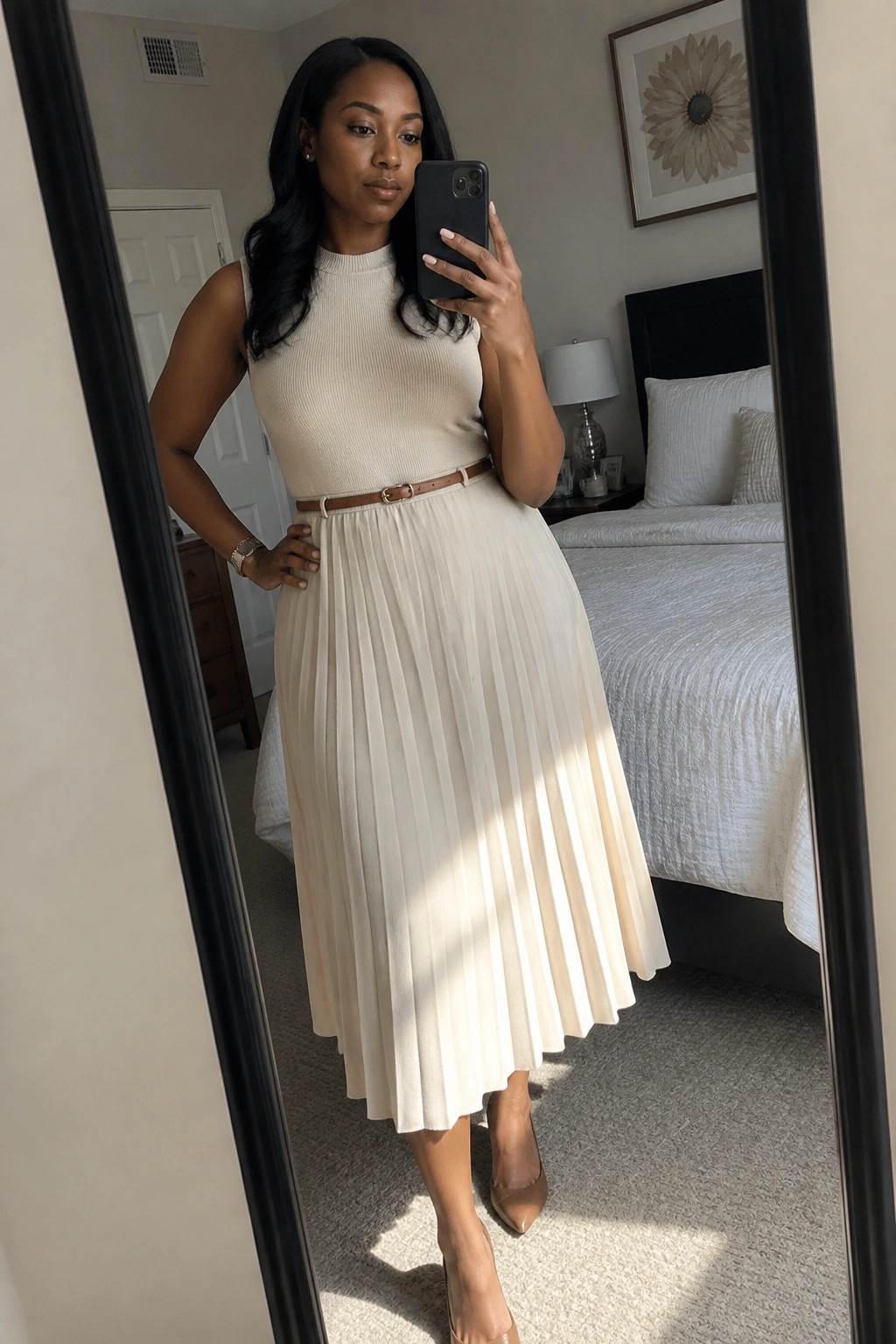 Woman in beige pleated skirt and top taking bedroom mirror selfie
