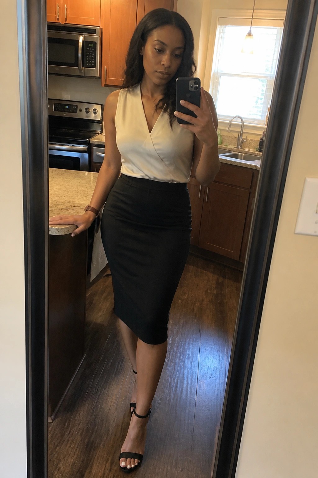 Woman in white wrap top and black pencil skirt taking kitchen mirror selfie