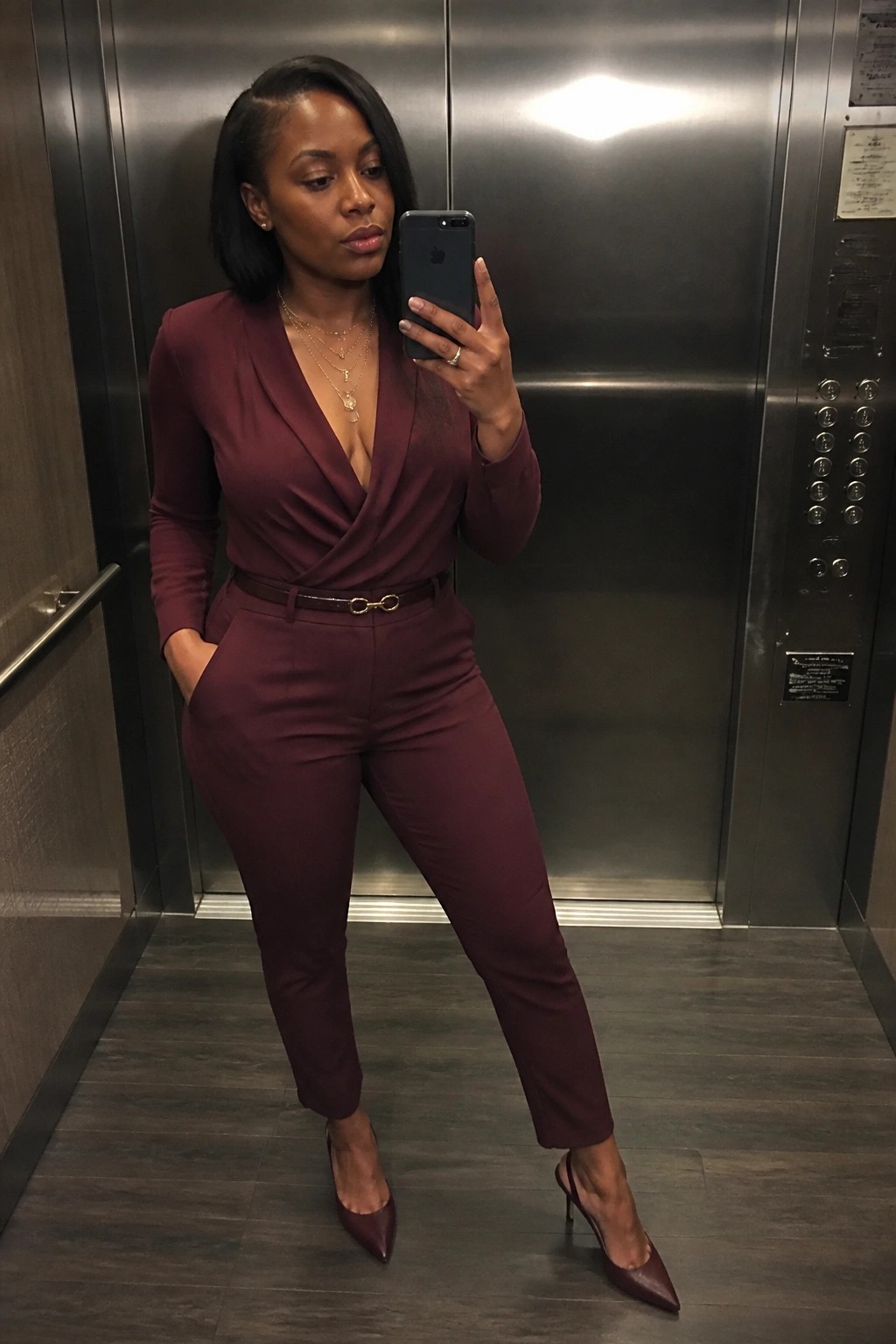 Woman in maroon pantsuit taking selfie with phone in elevator