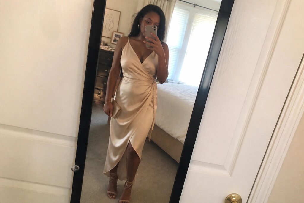 21 Elegant Outfits for Black Women That Elevate Special Occasions Woman in beige satin wrap dress taking mirror selfie holding phone and clutch