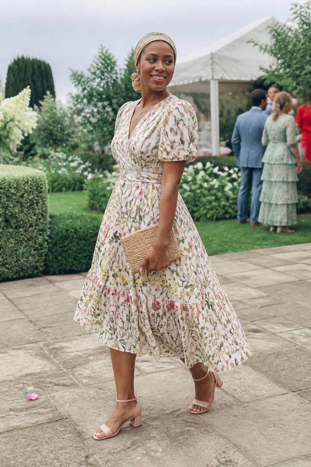 Woman in floral midi dress and headwrap holding woven clutch in garden