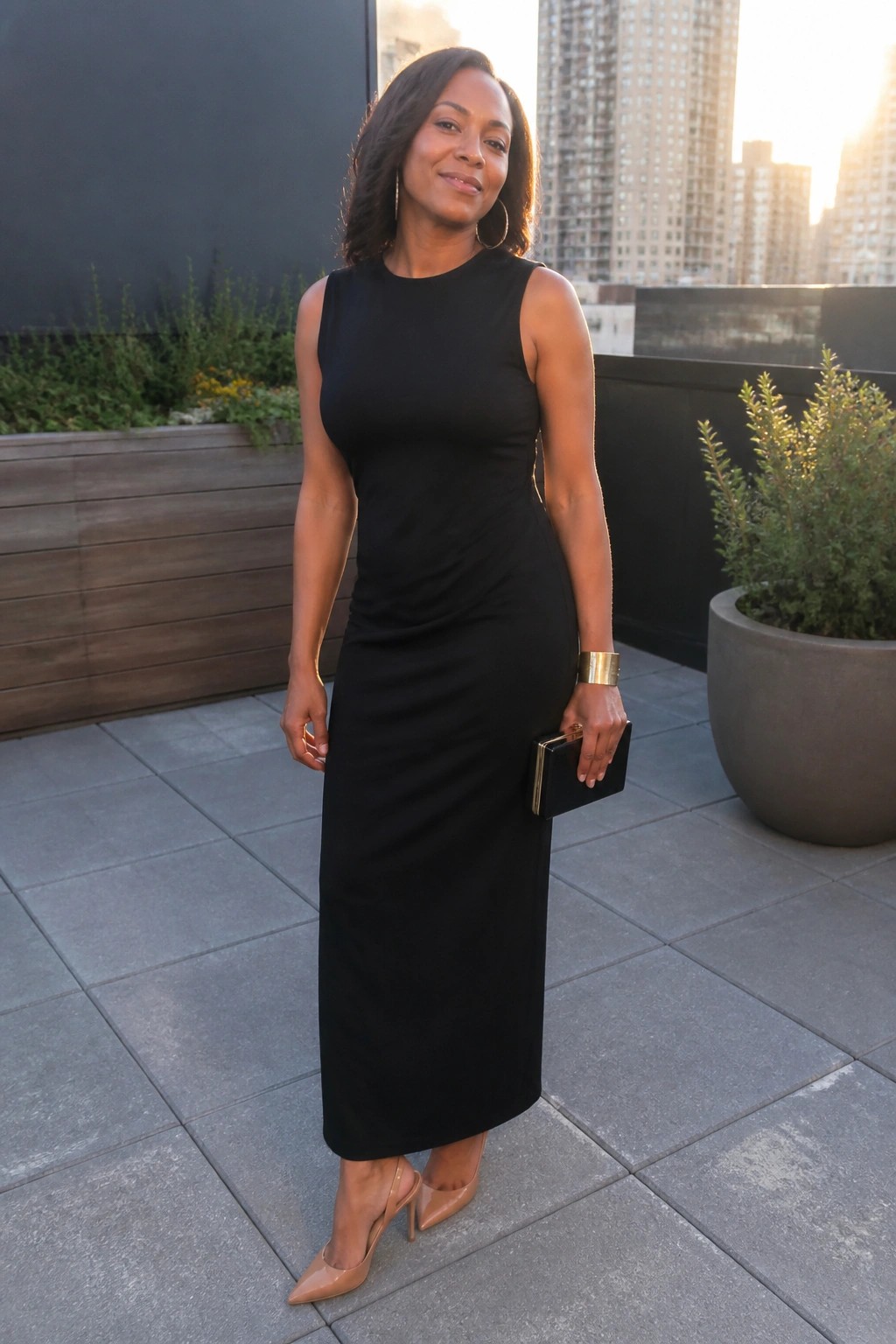 Woman in black sleeveless midi dress holding clutch on sunset rooftop