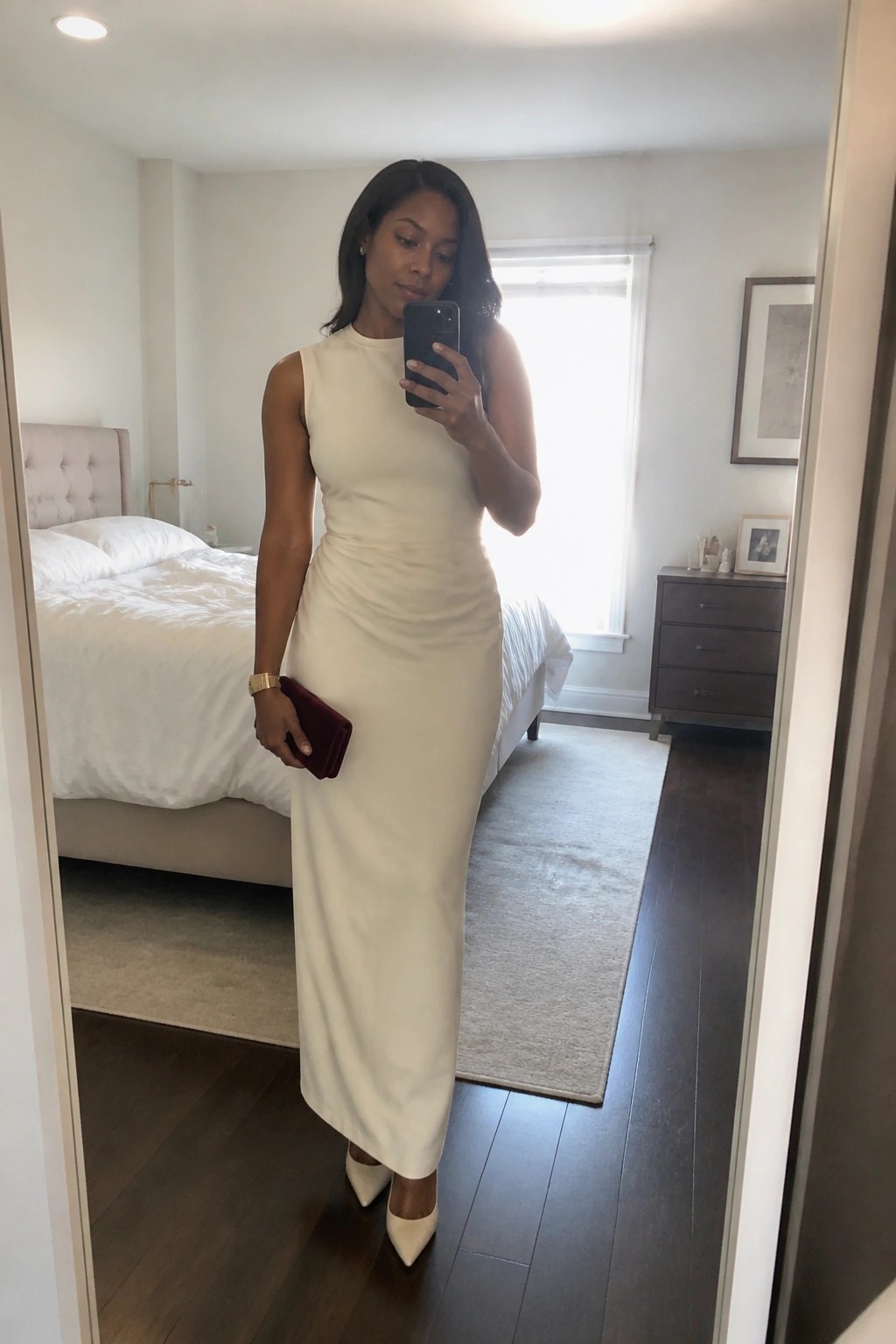 Woman in cream sleeveless maxi dress taking mirror selfie in bedroom