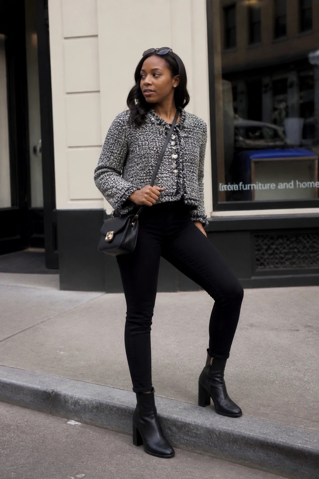 Woman in black-and-white tweed jacket and black jeans posing on sidewalk