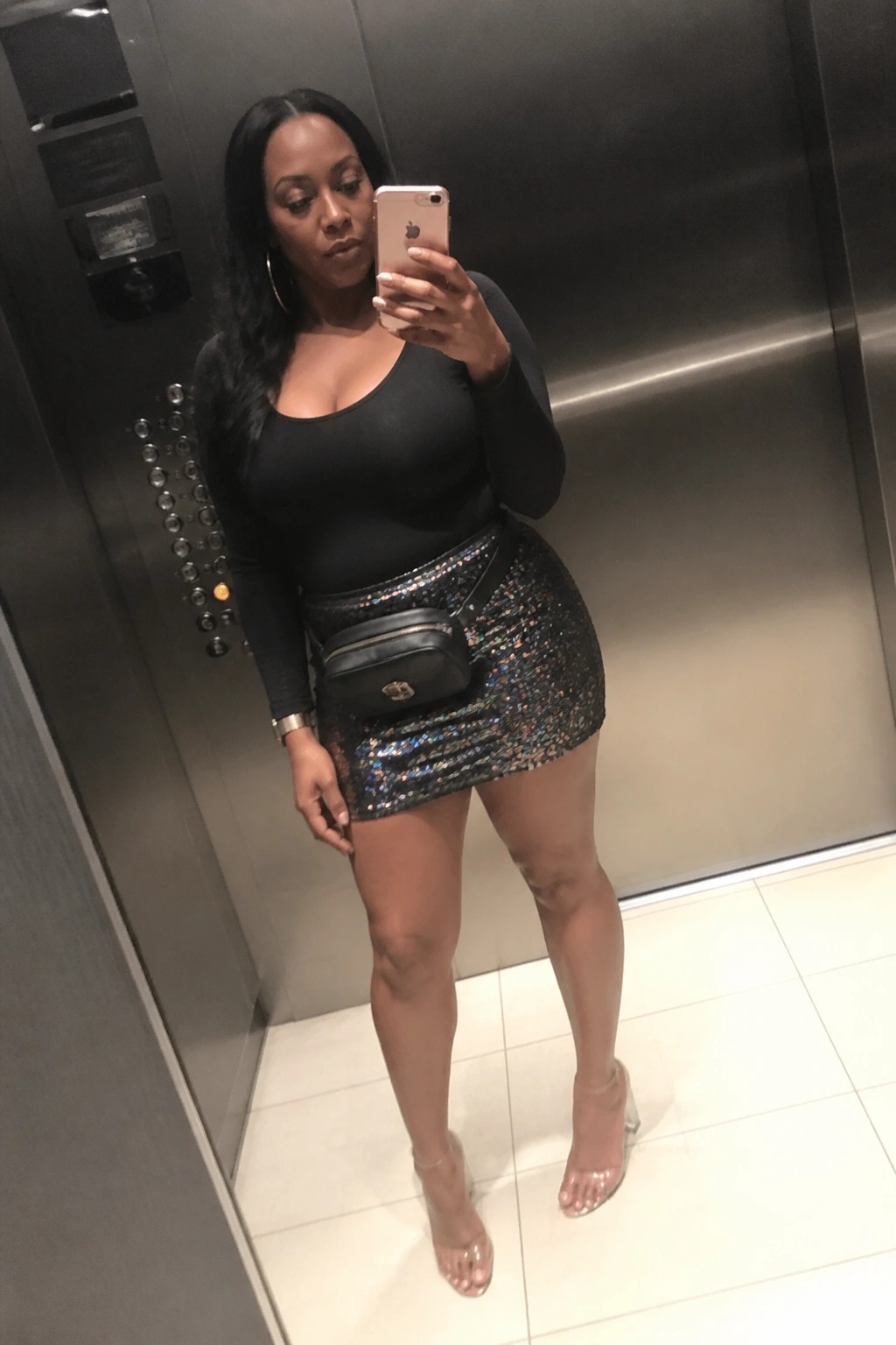 Woman in black top and sequined mini skirt taking selfie in elevator