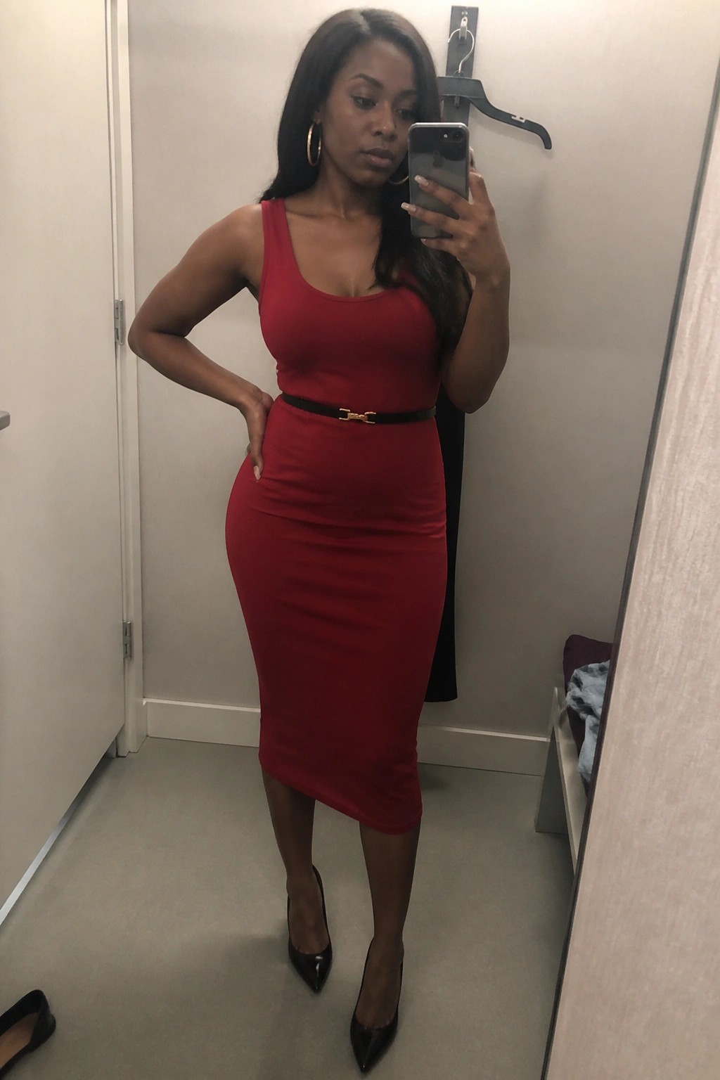 Woman in red midi dress with black belt taking mirror selfie in fitting room