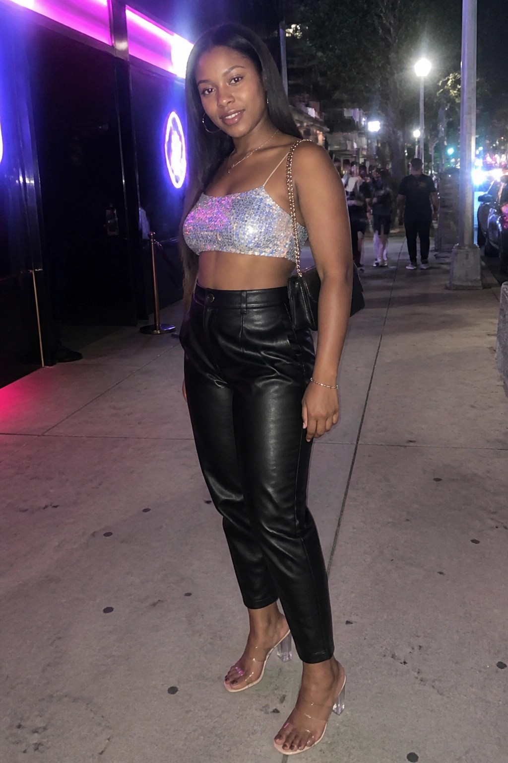 Woman in sequined crop top and black leather pants on nighttime city sidewalk