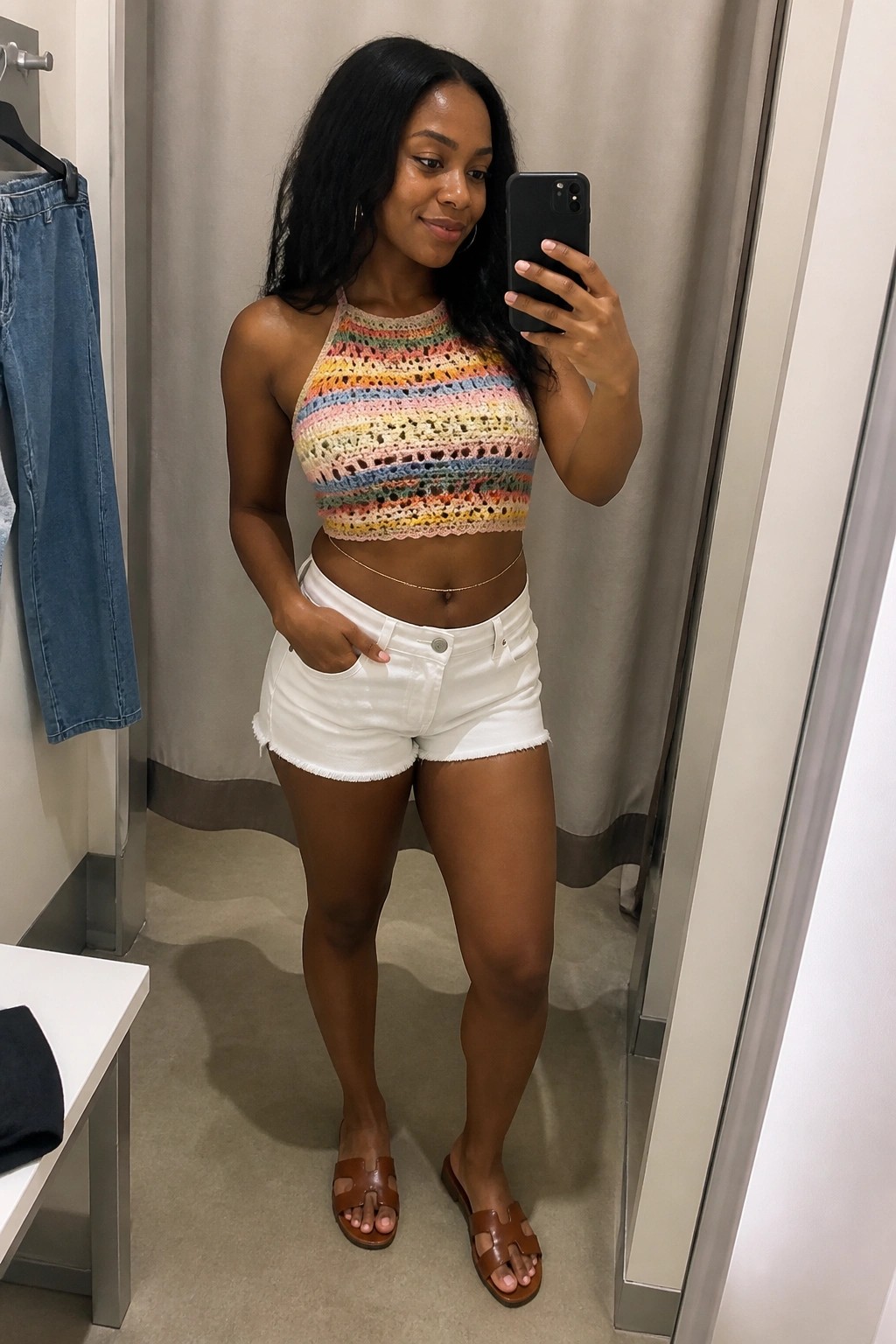 Woman in colorful striped crochet halter top and white shorts taking mirror selfie.