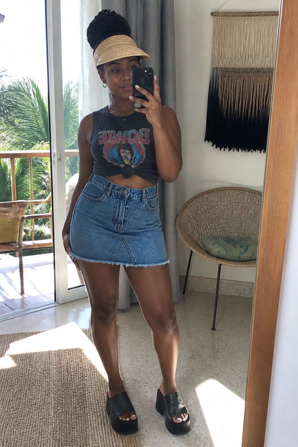 Woman in knotted Bowie tank top and frayed denim skirt taking mirror selfie
