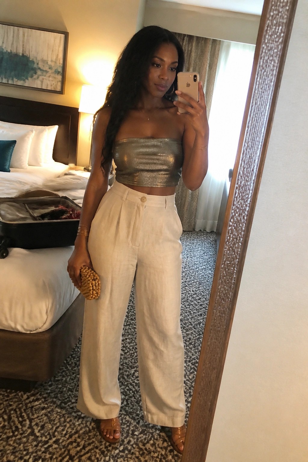 Woman in metallic gold strapless top and white wide-leg pants taking hotel mirror selfie