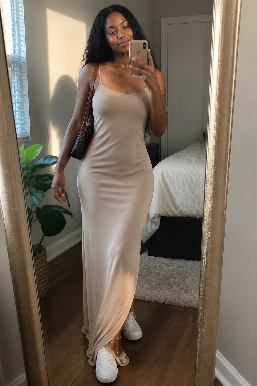 Woman in beige maxi dress and white sneakers taking mirror selfie in bedroom