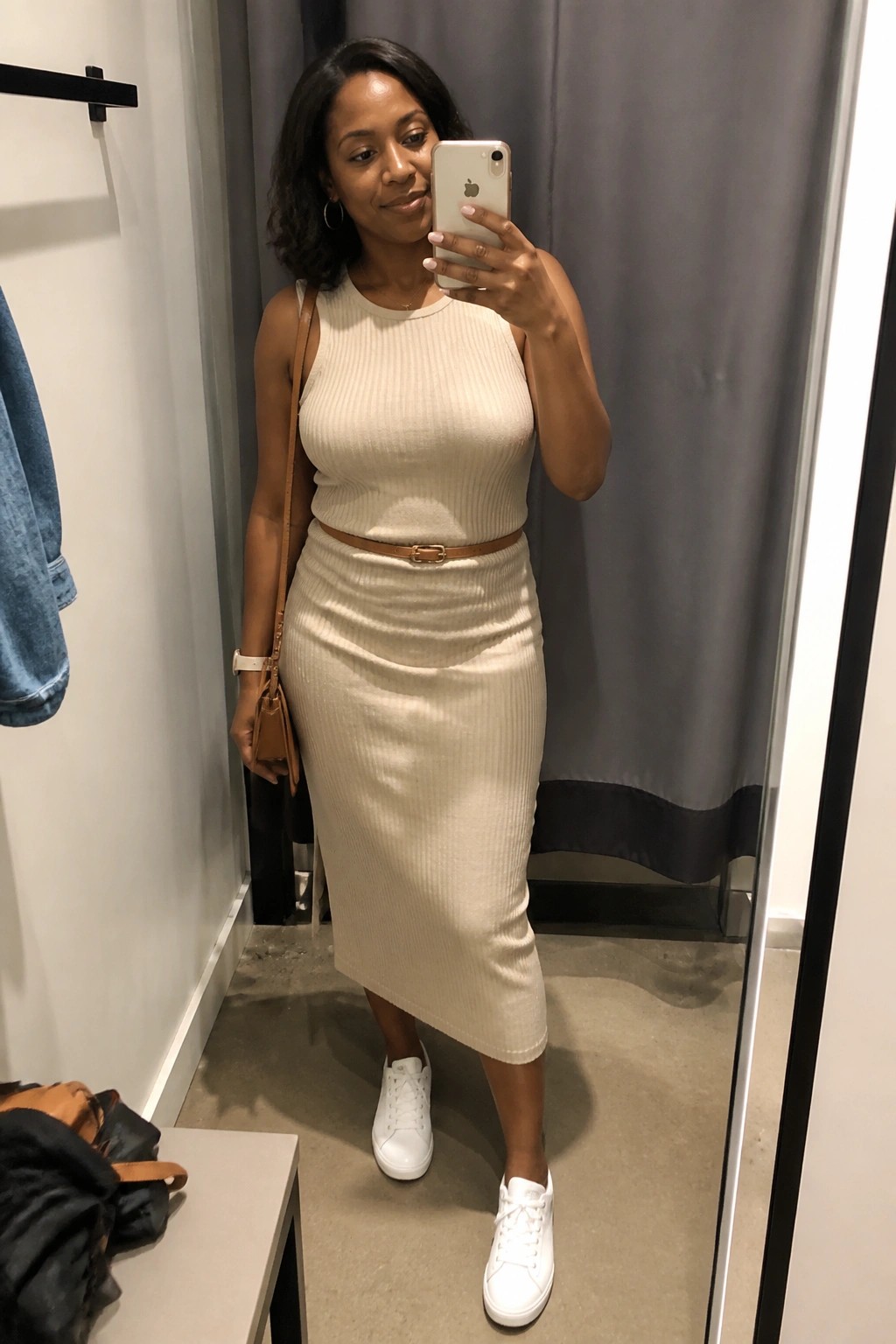 Woman in cream ribbed dress with brown belt taking mirror selfie in fitting room