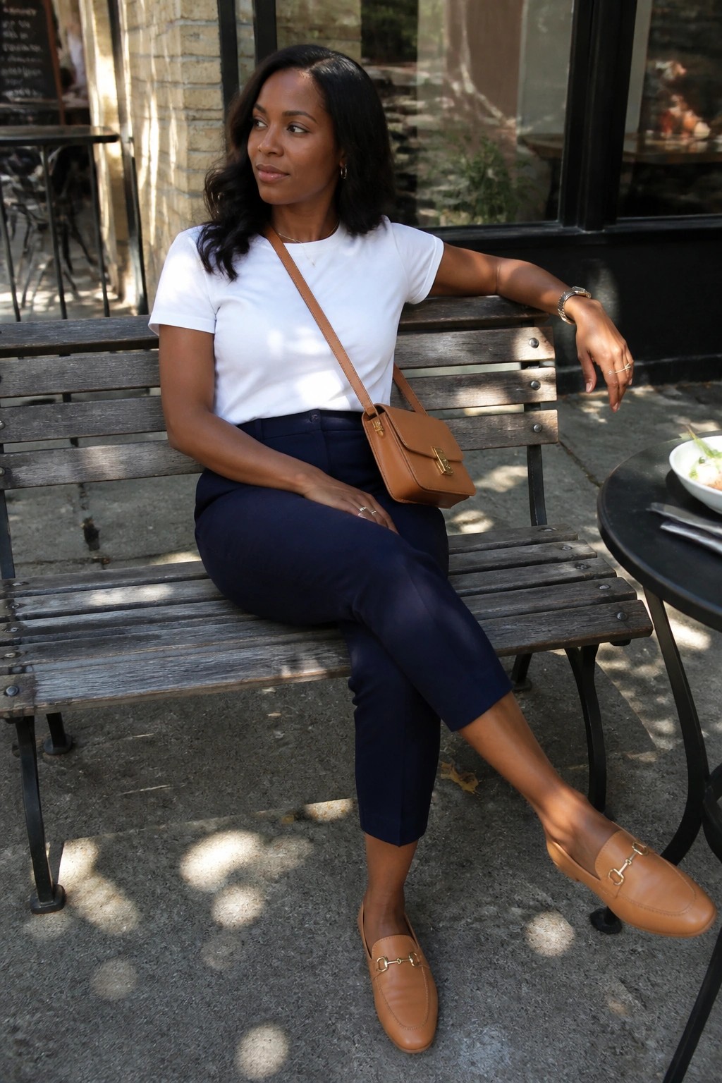 Woman in white t-shirt and navy pants on wooden bench with brown bag