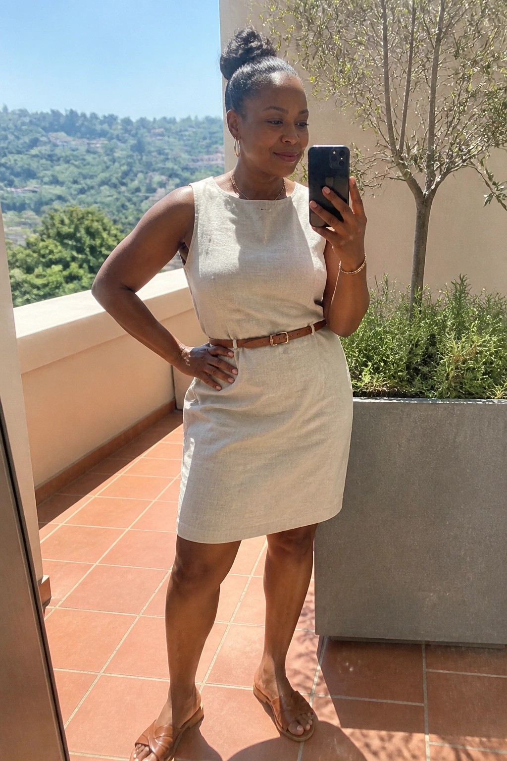 woman wearing cream linen sleeveless dress belted at waist with brown leather belt and matching slides