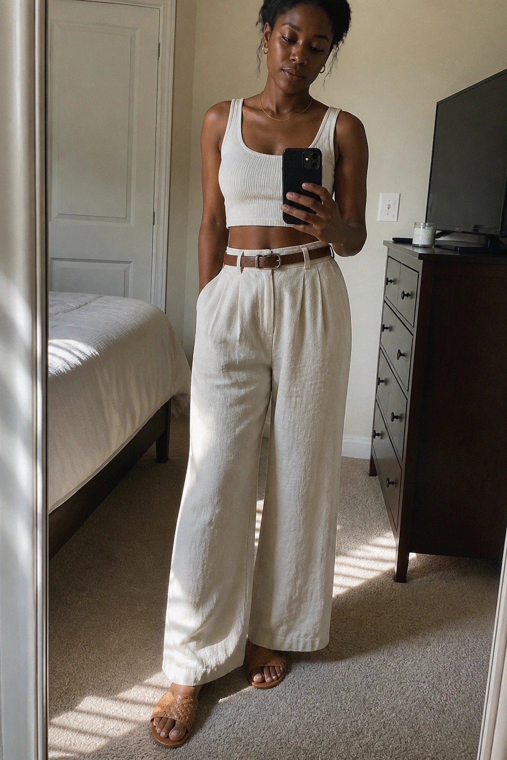 Woman in white crop top and wide-leg pants taking bedroom mirror selfie