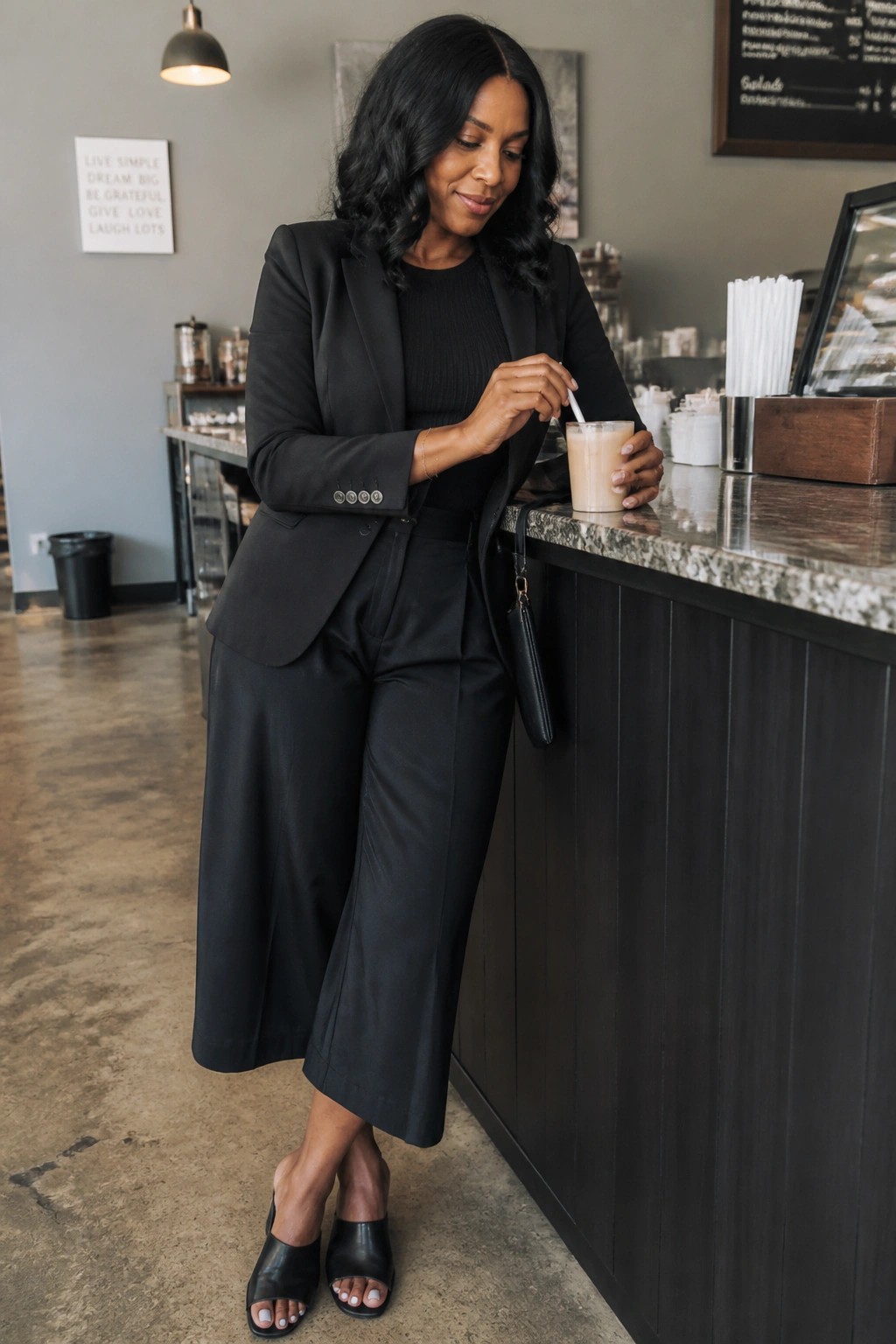 Woman in black blazer stirring iced coffee at cafe marble counter