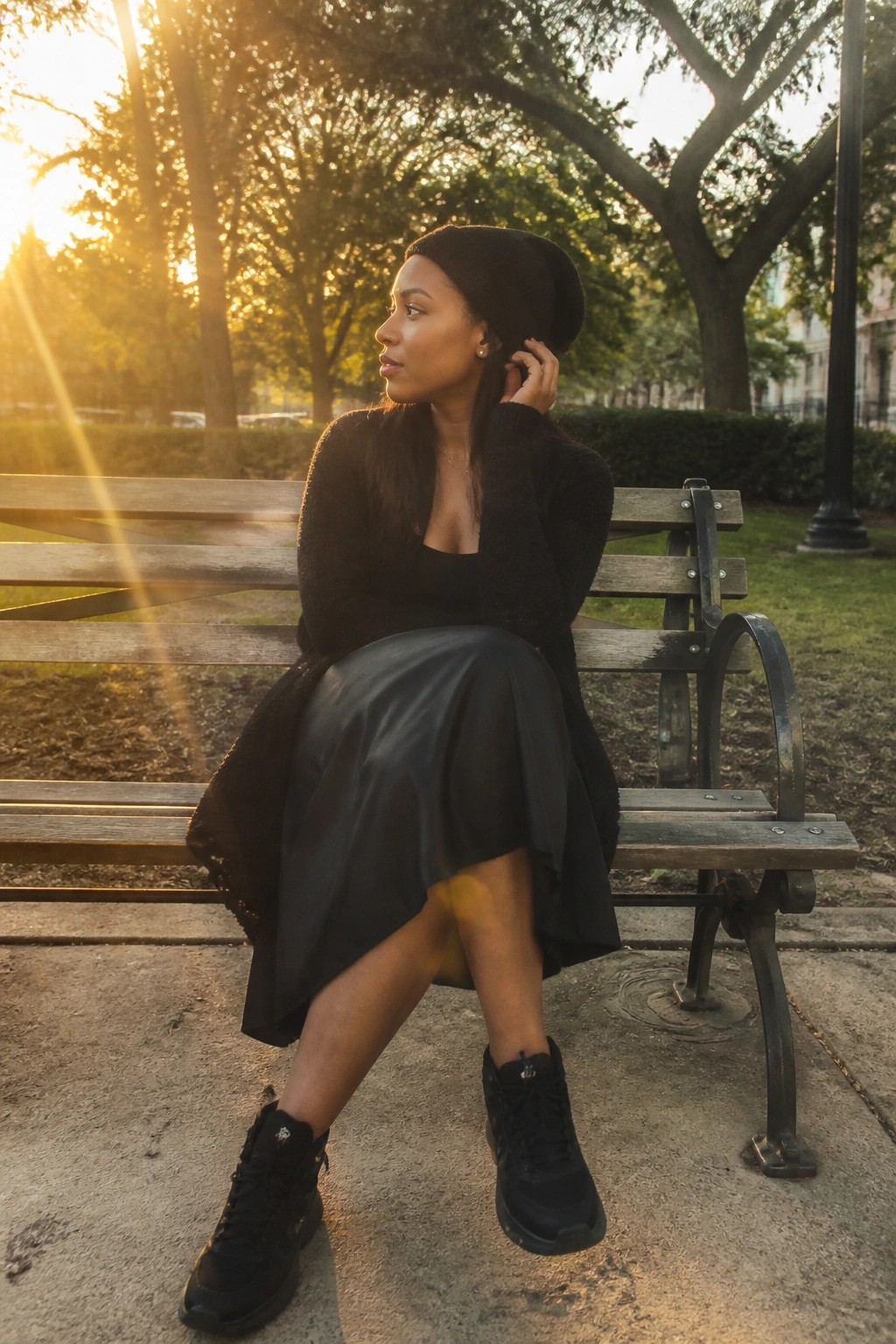 Woman in black beanie and skirt seated on park bench in golden sunlight
