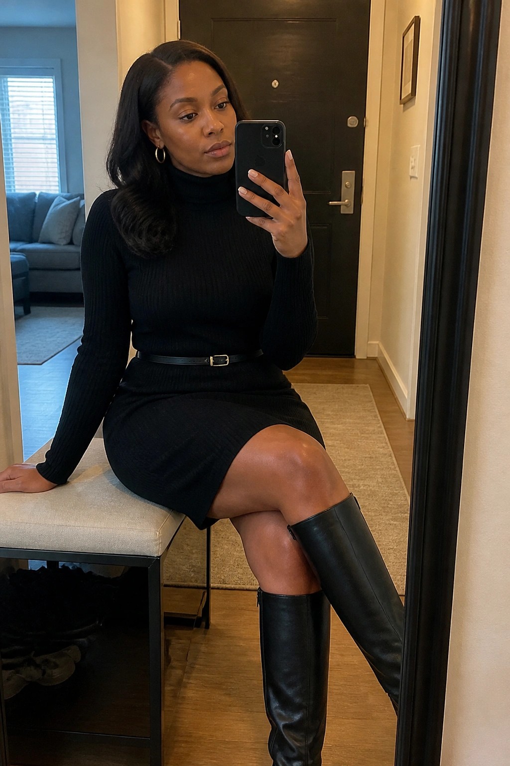Woman in black turtleneck dress and knee-high boots taking mirror selfie with phone