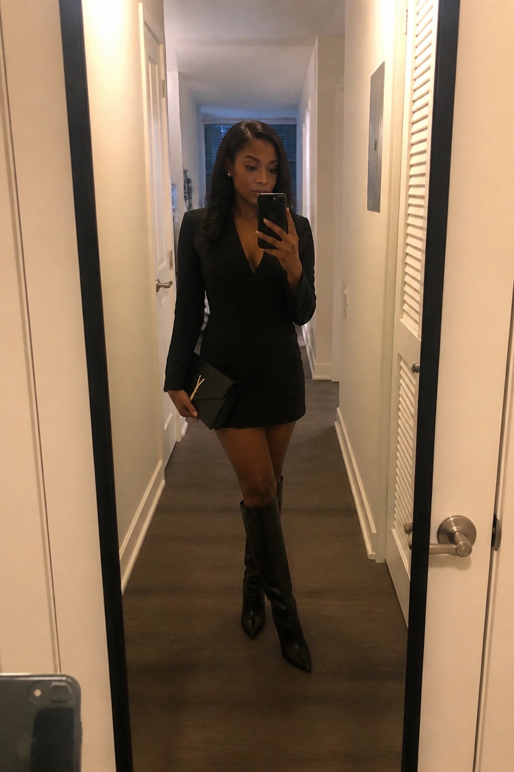 Woman in black blazer dress and boots takes mirror selfie in hallway