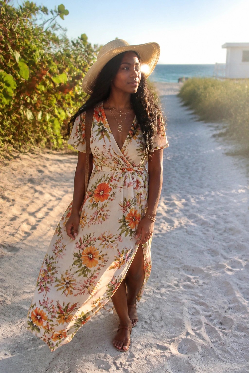 Woman in floral wrap dress and straw hat on sunny beach path
