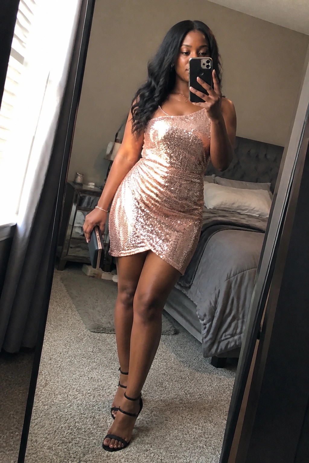 Woman in rose-gold sequin mini dress taking bedroom mirror selfie with phone