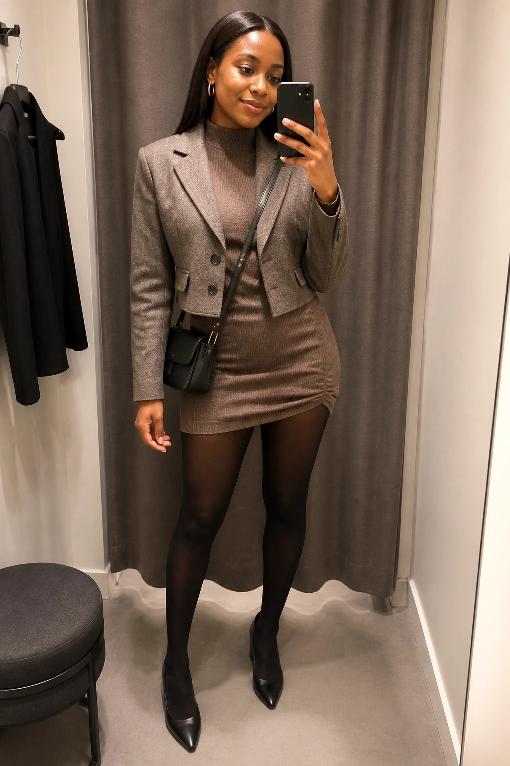 Woman in brown blazer and mini dress taking mirror selfie in fitting room
